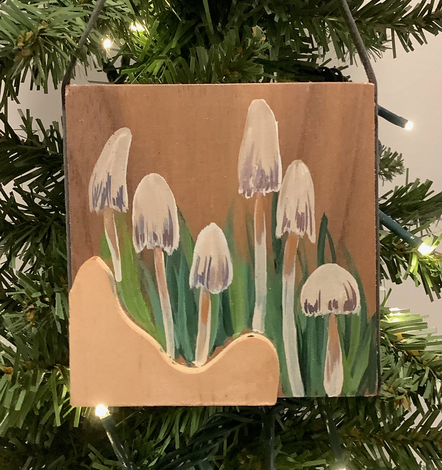 Wooden ornament with painted mushrooms hanging on a Christmas tree.