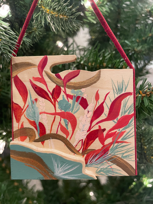 Decorative ornament with red and blue leaf design hanging on a Christmas tree.