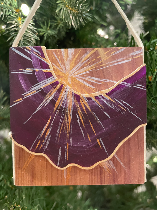 Decorative wooden ornament with a purple and gold design hanging on a Christmas tree.