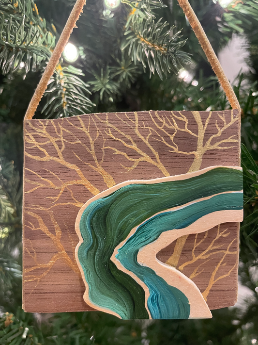Wooden ornament with wavy green and beige design hanging on a Christmas tree.